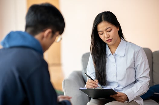 A female psychologist talks to a patient, listening to his symptoms and noting them in her clipboard photo
