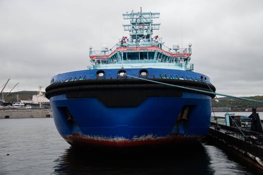 Large Blue Tugboat Docked at busy Shipyard under overcast Cloudy Sky. Visible Maritime infrastructure and Industrial background add context to Vessel's functional role in Port operations photo