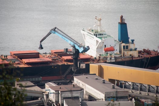 Industrial Port large Cargo Ship docked Freight Terminal. Blue Gantry Crane transferring goods from Vessel. Warehouses and calm Harbor water surface background, indicating busy maritime Logistics Hub photo