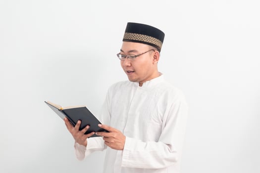 Asian Muslim man wearing white clothes reading quran during Ramadan Eid Al Fitr and eid adha days celebration isolated white. Islamic celebration concept. photo