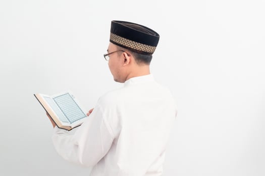 Back side Asian Muslim man wearing white clothes reading quran during Ramadan Eid Al Fitr and eid adha days celebration isolated white background. Islamic celebration concept. photo