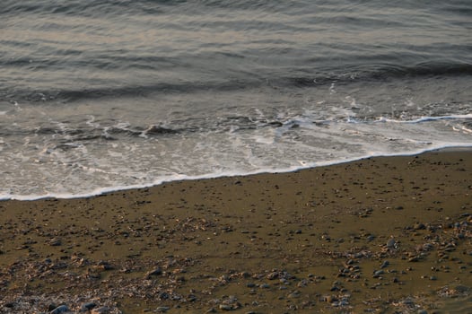 Waves gently lap against the rocky shoreline at dusk in a tranquil coastal landscape photo