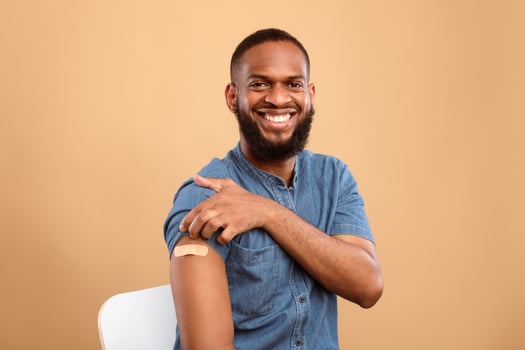 Antiviral immunization. Cheerful vaccinated African American man showing shoulder with medical band aid after flu vaccine shot, posing after flu vaccination, beige studio background photo