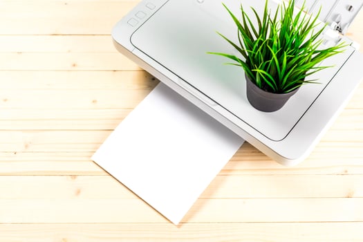 Modern printer with a small green plant on top amidst a wooden workspace during the day photo