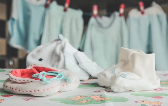 Adorable baby booties, a hat, and soft baby clothes drying in the background. photo