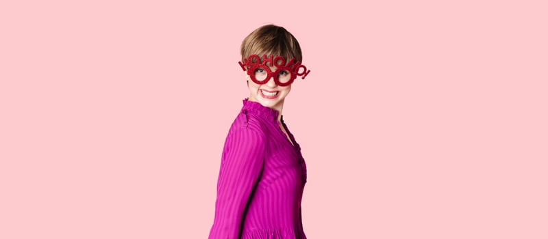 A cheerful young woman in Christmas glasses poses on a highlighted pink background. photo