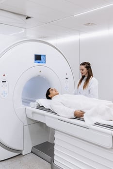 Female doctor is preparing patient for magnetic resonance procedure. Patient is lying at CT scanner bad and waiting to be scanned. Medical Lab with High-Tech Equipment. Vertical shot photo