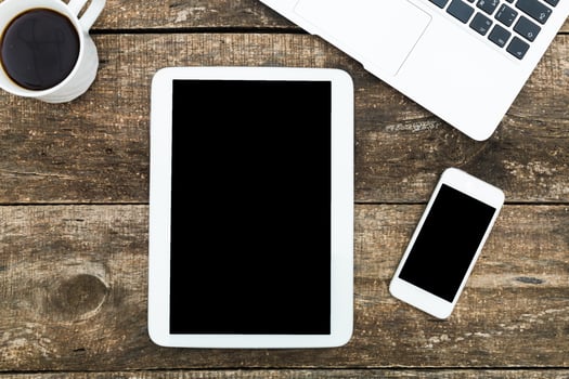 Desk setup featuring tablet, smartphone, laptop, and coffee cup on rustic wooden surface during daytime photo