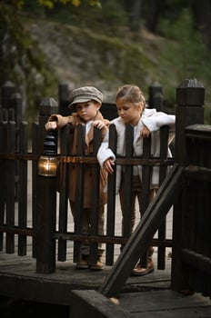 dressed in old fashioned clothes a boy and girl stand on a rustic wooden bridge with a light in hands photo