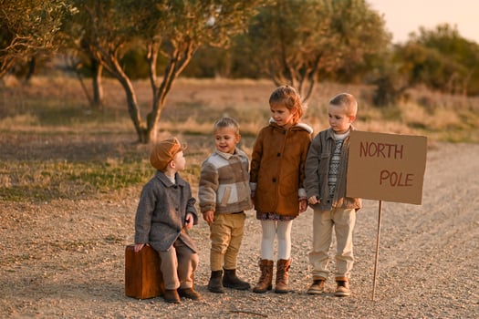 The children stand on the road next to a vintage suitcase and a North Pole sign, waiting for a ride. photo