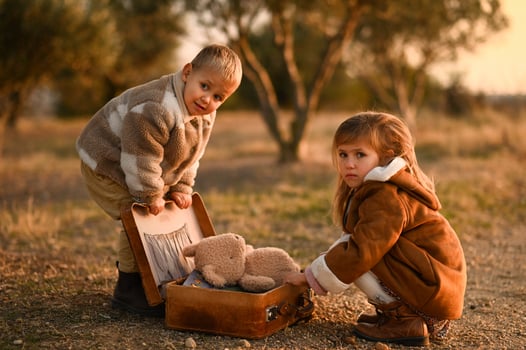 A boy and a girl sit over an old suitcase, where they have packed their teddy bear and books. photo
