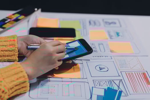 A person is using a cell phone while sitting at a table with a laptop photo