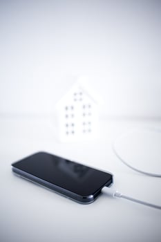 Smartphone charging by miniature house on white background photo