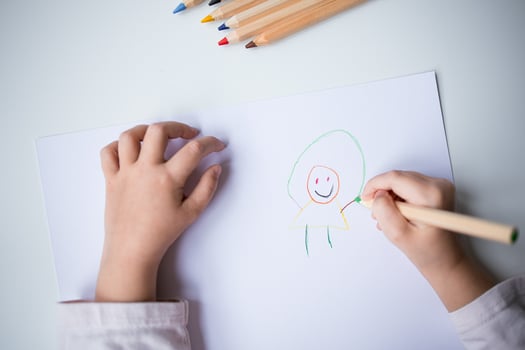 Child drawing colorful smiley figure with pencils on white paper photo