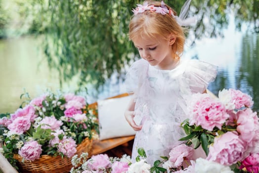 Portrait of a cute little girl in an elegant dress on a wooden boat among pink peonies on the pond or lake. photo