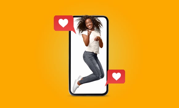 A young woman with curly hair jumps joyfully, holding a smartphone. Colorful hearts pop up beside her, symbolizing the excitement of love and connection through social media. photo