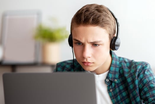Closeup of concentrated schooler with headset studying online from home, using laptop, empty space photo