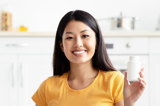 Happy young asian lady sitting on kitchen floor with cute long coat doggy jack russel terrier, showing white jar with supplements or vitamins for domestic pets, panorama with copy space photo