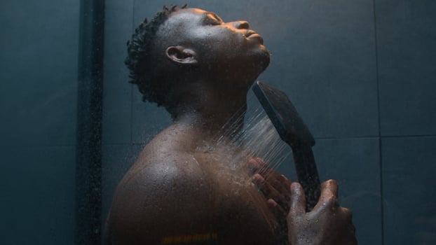 Handsome sexy guy man taking shower at dark modern home bathroom washing cleaning rinsing muscular body gel falling hot water bath hygiene routine refreshment morning energy relaxing after gym workout photo