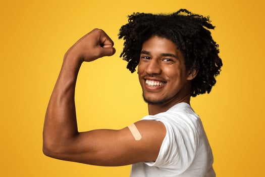 Excited African American Man Showing Arm With Plaster After Getting Covid-19 Vaccination, Happy Vaccinated Black Guy Demonstrating Biceps With Adhesive Band, Posing Over Beige Studio Background photo