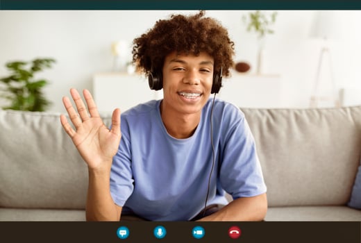 Head shot of smiling black teenager wearing headphones, waving hand to webcam, greeting teacher during remote lecture or online course, having call, computer screen view photo