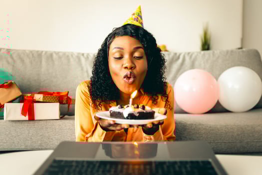 Happy Birthday. Black Lady Blowing Candle On Cake In Front Of Laptop Computer Celebrating Her Holiday Remotely, Having Virtual Party Via Call At Home. Modern B-Day Celebration photo