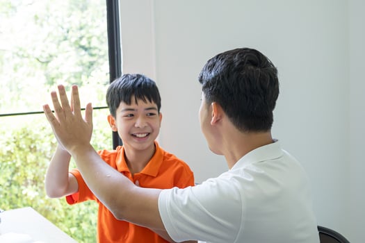 a man and boy are sitting at a table with their hands up photo