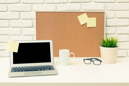 Modern workspace with laptop, coffee cup, and plant on a clean white desk against a brick wall photo