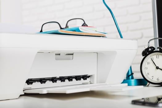 Office workspace with printer, glasses, books, and clock resting on a desk during the day photo