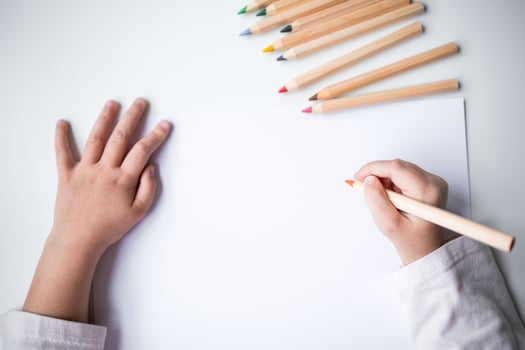 Childs hands drawing with colored pencils on white paper photo