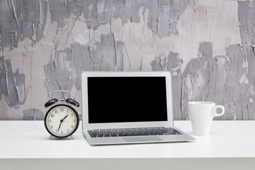 Desk setup with a laptop, alarm clock, and coffee cup in a modern workspace setting photo