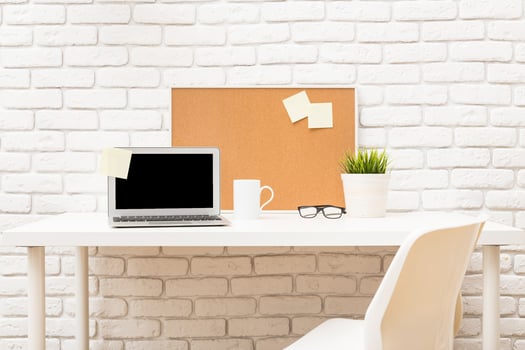 Modern workspace featuring a laptop, coffee cup, and plant against a white brick wall during daytime photo