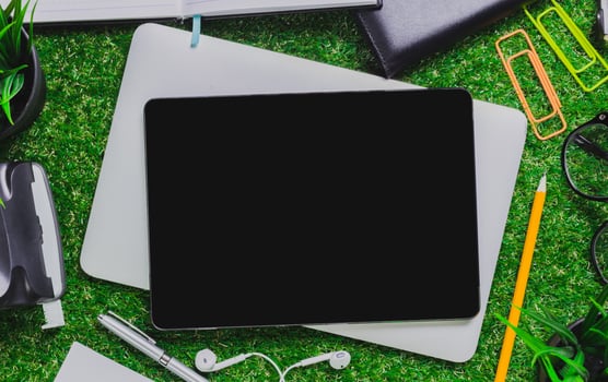 Digital workspace with tablet, stationery, and stationery items on green grass background photo
