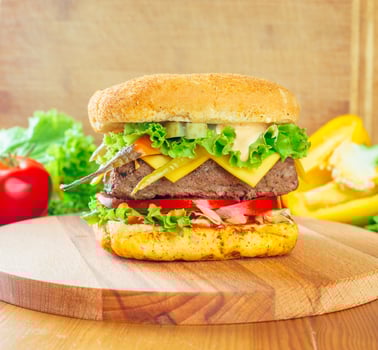 Juicy burger stacked with fresh vegetables and melted cheese served on a wooden board photo