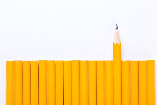 Yellow pencils arranged in a neat row with one pencil standing out against a white background photo