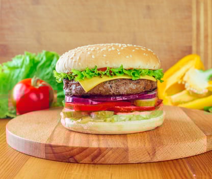 Freshly made cheeseburger with lettuce, tomato, and pickles on a wooden cutting board photo