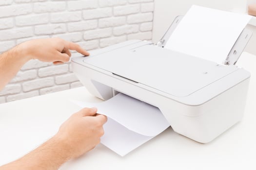 Person using a printer to retrieve a freshly printed document in a bright workspace with a brick background photo