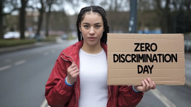 A woman with braided hair holds a cardboard sign reading Zero Discrimination Day, advocating for equality at city street photo