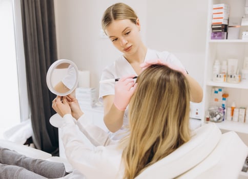 Cosmetologist making injection into female forehead with syringe for wrinkles smoothing, patient looking in mirror during procedure in beauty clinic photo