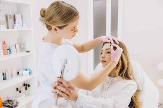 Beautician marking injection points on woman's forehead before botox treatment in aesthetic medicine clinic photo