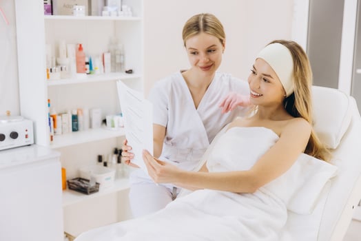 Beautician holding document and explaining treatment plan to smiling young woman in beauty salon photo