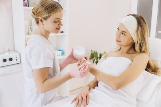 Beauty professional applying moisturizing cream to blonde client reclining during skincare treatment in spa setting photo