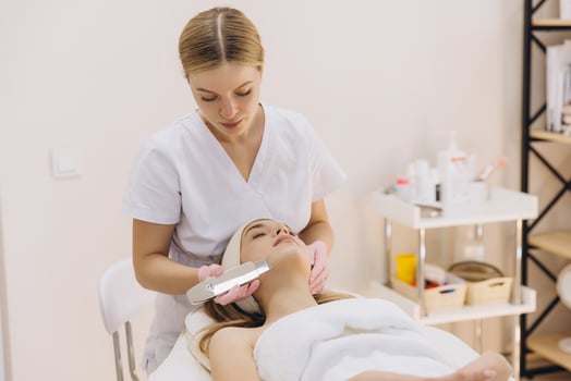 Professional beautician using ultrasonic scrubber for facial peeling procedure on young woman lying on couch in beauty salon photo