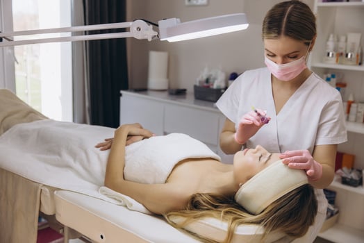 Cosmetologist making rejuvenating facial injections for young blond woman lying on a couch in a beauty salon photo