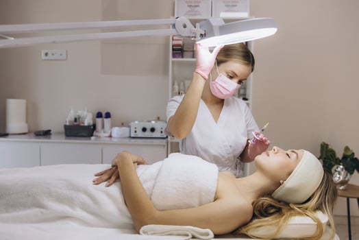 Cosmetologist adjusting lamp and giving hyaluronic acid injection to young blonde woman for facial rejuvenation in beauty salon photo