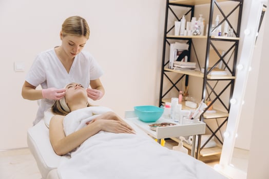 Pink gloved beautician spreading facial mask on relaxed client during professional skincare treatment at spa photo