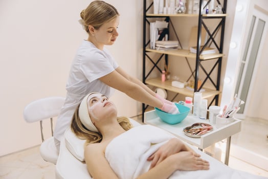 Beautician wearing gloves preparing cosmetic mask for her client lying on massage table in beauty salon photo