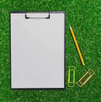 Blank clipboard with stationery items on green grass during sunny afternoon photo