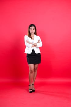 full length young indonesia office woman wearing elegant white coat arms folded looking at camera, standing isolated red background. for corporate, business, fashion content photo