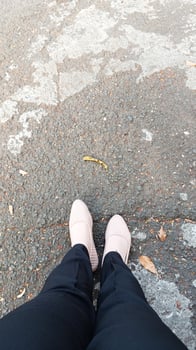 A woman's feet in flat shoes and black trousers on the side of the road. photo